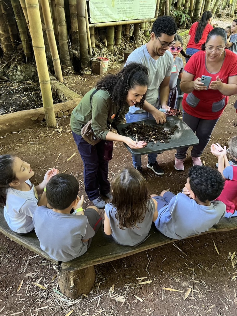Educadora mostra minhocas da compostagem para grupo de crianças em vivência de ecopedagogia