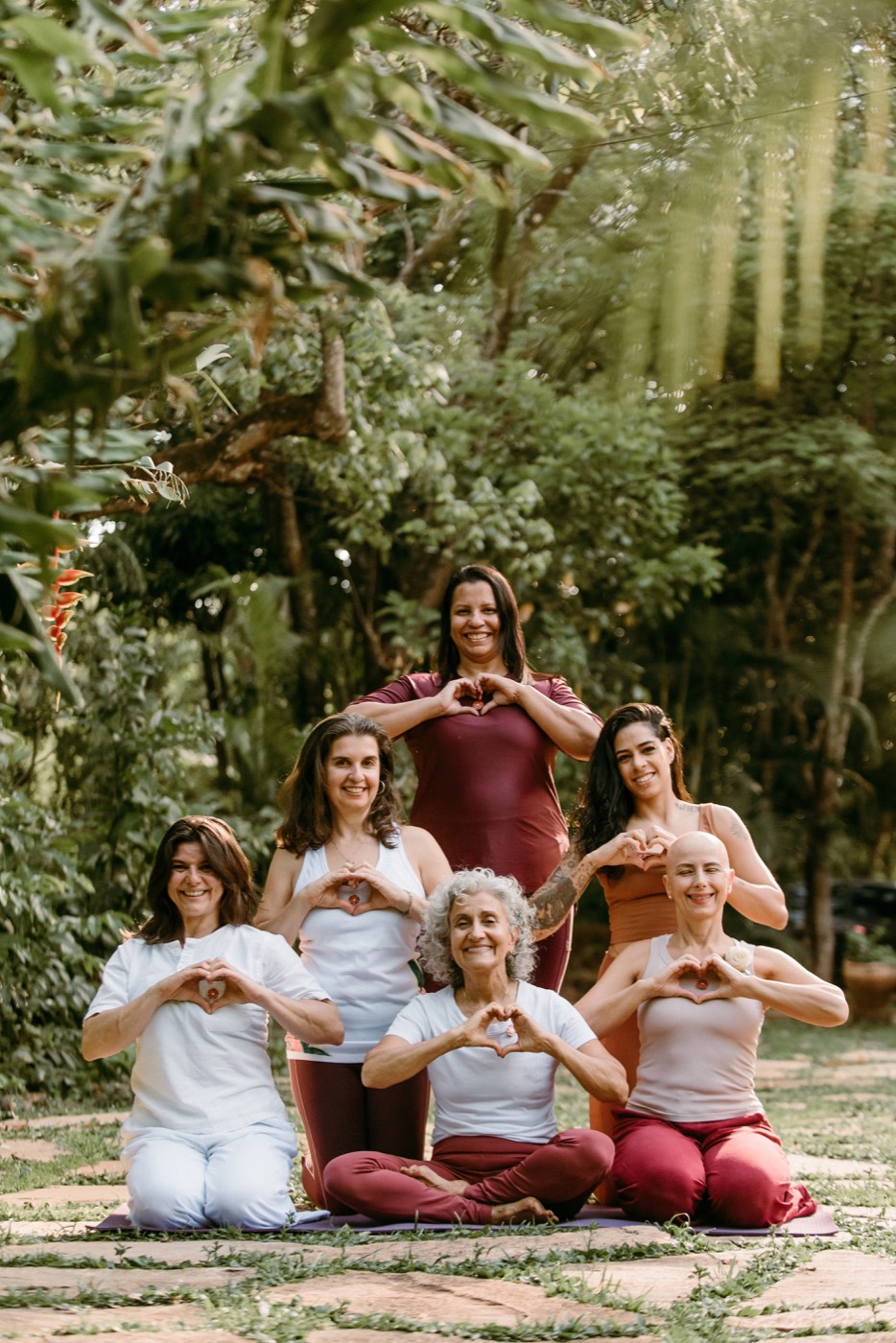 Grupo de yoga reunido fazendo coração com as mãos ao ar livre no Sítio Geranium