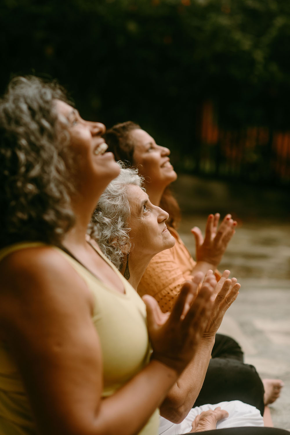 Mulheres praticando yoga ao ar livre, sorrindo com as mãos em oração