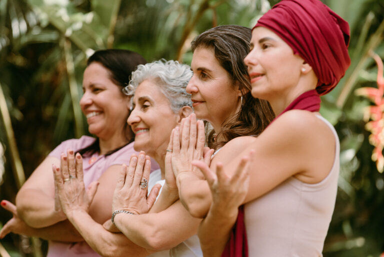 Quatro mulheres em fileira com as mãos em oração durante prática de yoga
